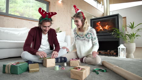 couple wrapping christmas gifts by cozy fireplace, wearing festive headbands