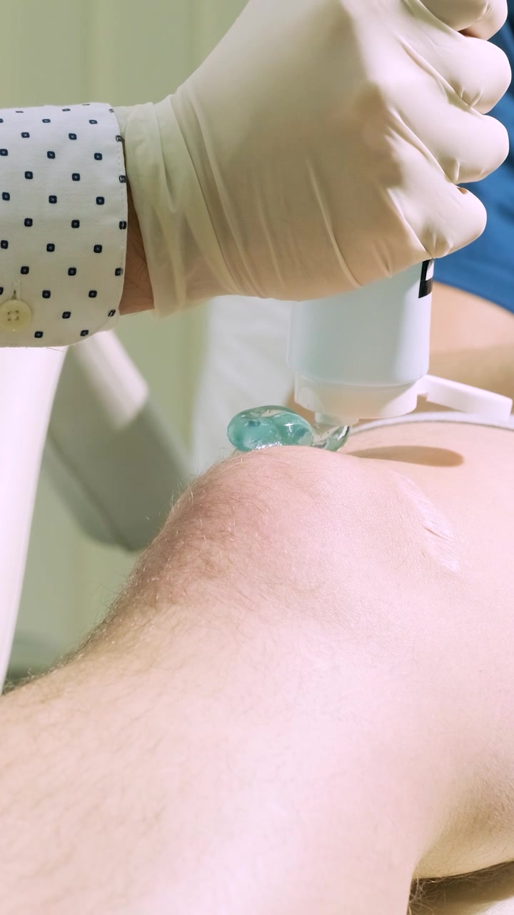 Professionista medico che applica gel per ecografia sul ginocchio di un paziente