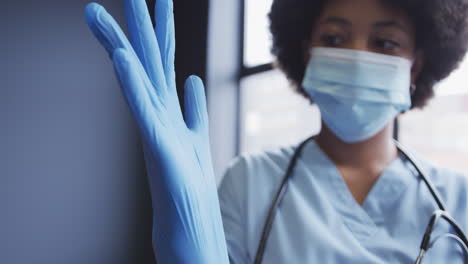 biracial female doctor wearing face mask putting protective gloves on