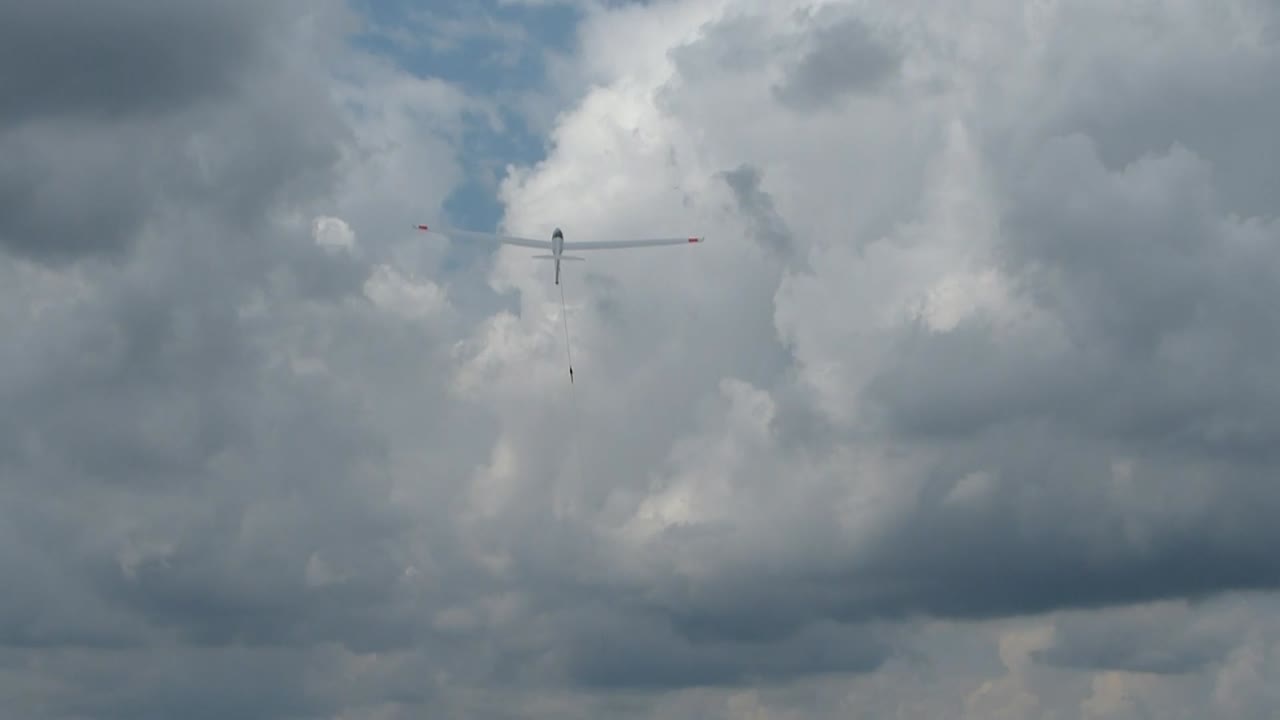 Zoom on white glider from behind being pulled up into the white cloud with a winch