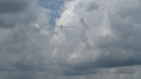zoom on white glider from behind being pulled up into the white cloud with a winch