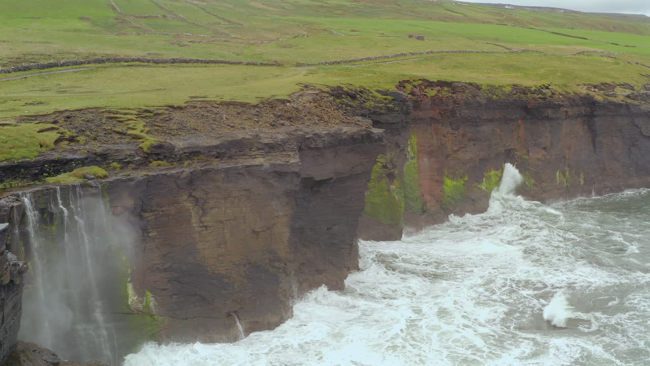 Static shot of waves crashing against Cliffs of Moher, Doolin, with sea spray rising high from impact