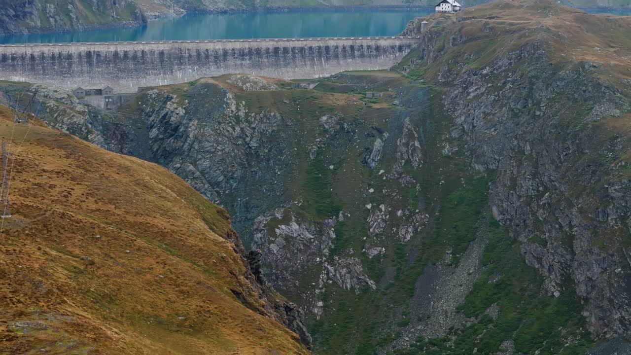 Aerial drone push in tilt up revealing a house and a vibrant blue reservoir in Cervinia, Italy, surrounded by striking alpine scenery and colorful water