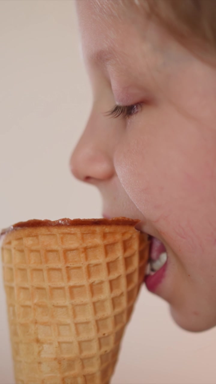 Close up of young girl eating ice cream cone. sequence shows progression of her face as girl takes bites with focus on texture detail and soft lighting against plain background