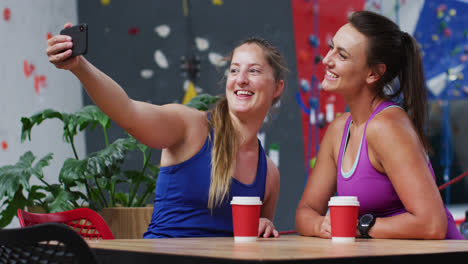 Zwei-Glückliche-Kaukasische-Frauen-Machen-Selfie-Mit-Smartphone-Im-Café-An-Der-Indoor-Kletterwand