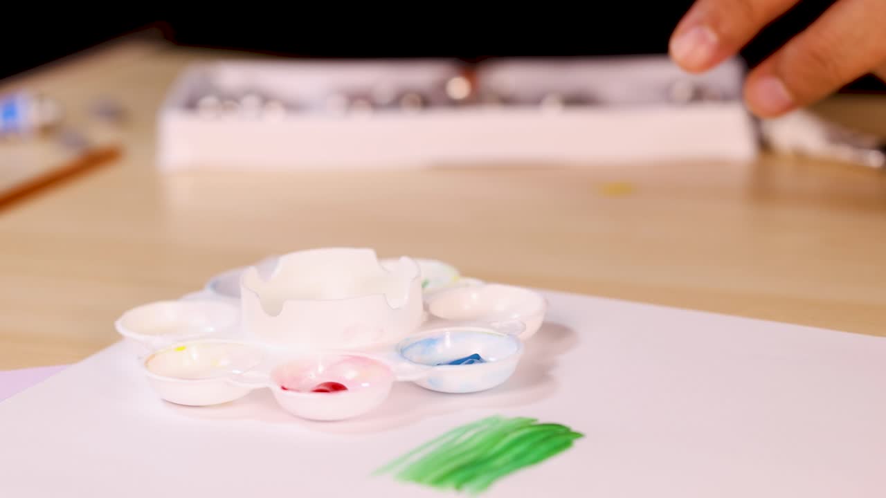 Artist hand mixes yellow watercolor paint on palette, close-up, warm lighting, shallow depth of field