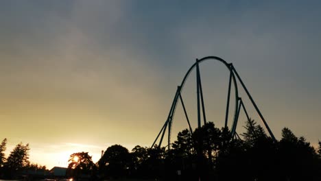 roller coaster thrill ride during sunset backlit by sky silhouette in amusement theme park 60fps 4k