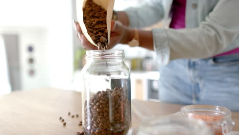 pouring coffee beans into glass jar, woman preparing fresh coffee at home