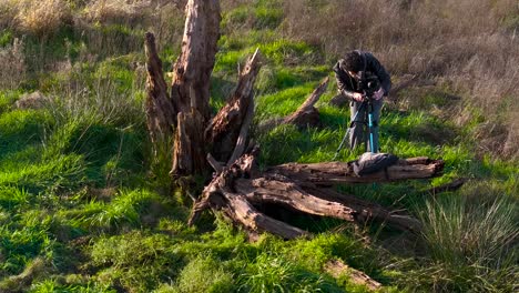 Fotógrafo-Al-Aire-Libre-Con-Cámara-Y-Trípode-Junto-A-La-Madera-De-Los-árboles-Muertos-En-El-Campo