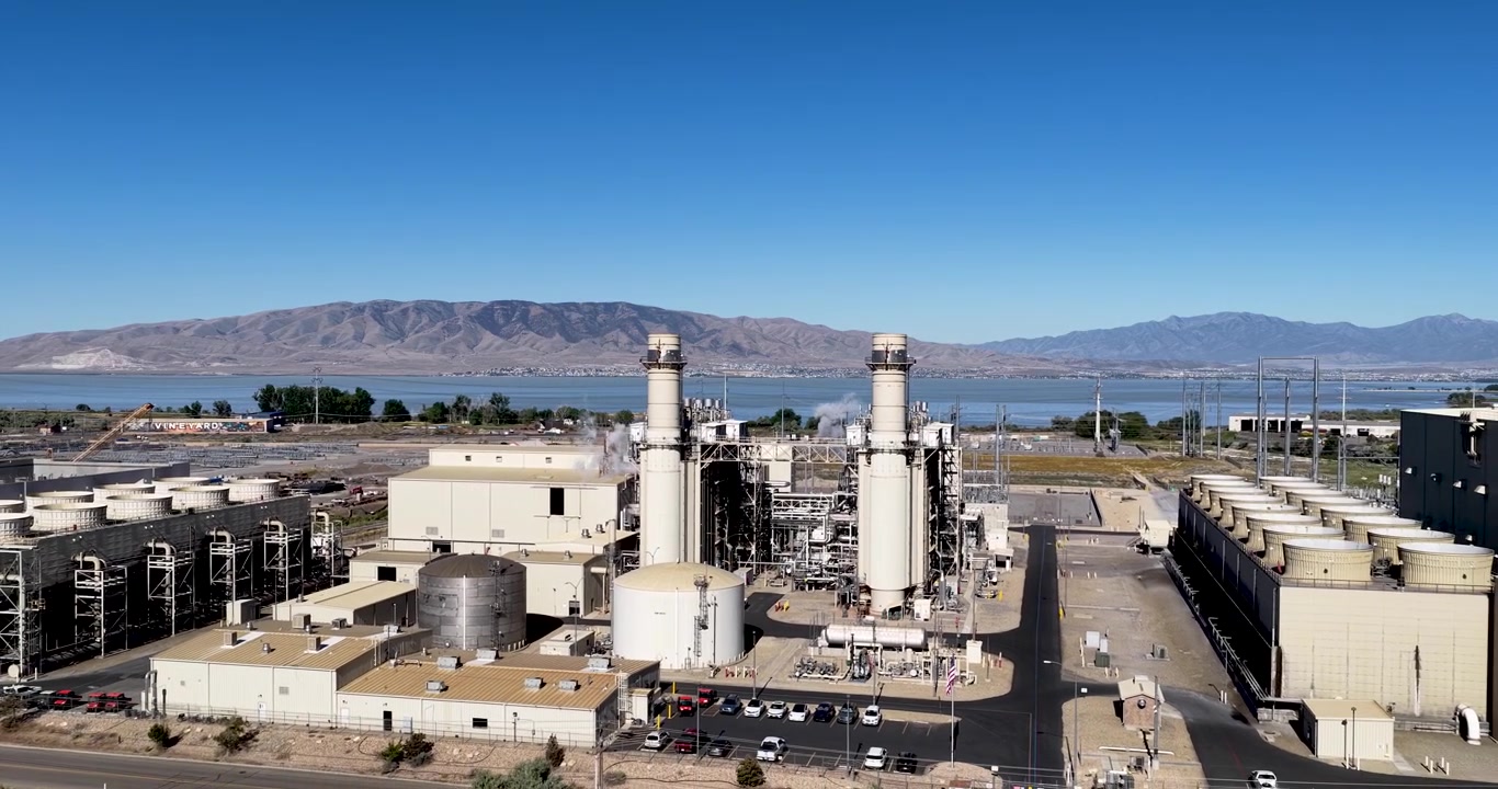 Large process manufacturing facility beside Utah Lake in Lindon, Utah, smokestacks, industrial piping, utility infrastructure and adjacent construction near Utah Lake Mountains, drone pullback reveal