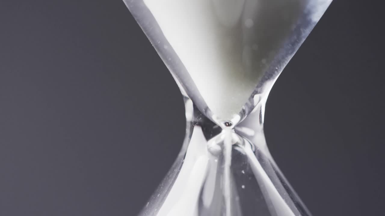Video of close up of hourglass with sand pouring, copy space on black background