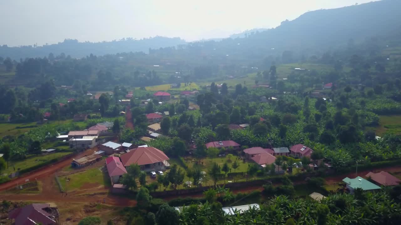 Drone orbit of a guesthouse complex with red roof and manicured gardens nestled in a lush green rural setting in Kapchorwa, Uganda, with trees, banana plants and gentle hills all around