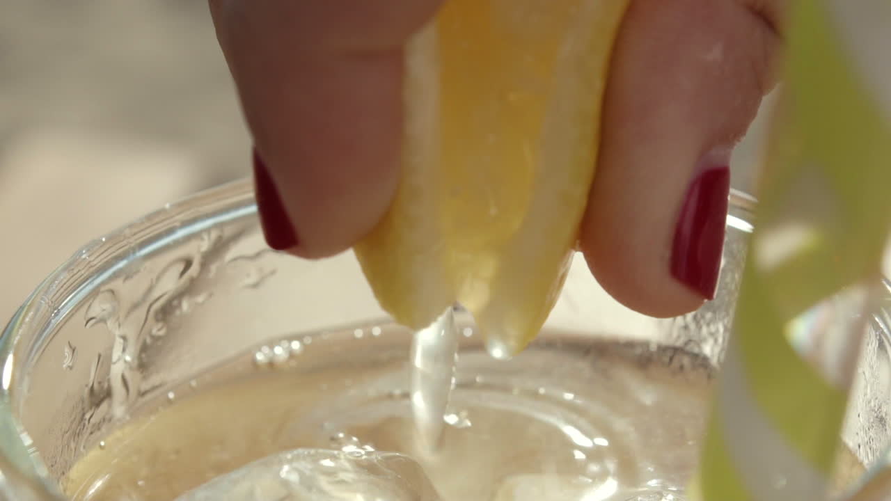 Primerísimo primer plano de un limón siendo exprimido en una bebida con pajita en cámara lenta, en un día soleado.