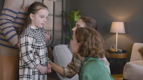 Niña-Pequeña-Hablando-Con-Su-Madre-Y-Su-Tía-Mientras-La-Abuela-La-Abrazaba-Por-Detrás-Durante-Una-Reunión-Familiar-En-Casa