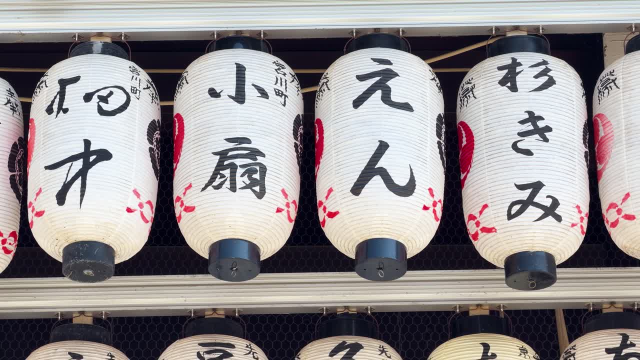 Inquadratura media fissa di lanterne di carta bianche con calligrafia kanji nera in un santuario di Kyoto