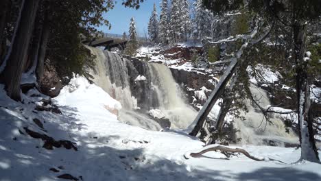 cascading waterfall and snow-covered trail at gooseberry falls state park on winter day. minnesota, usa. static shot