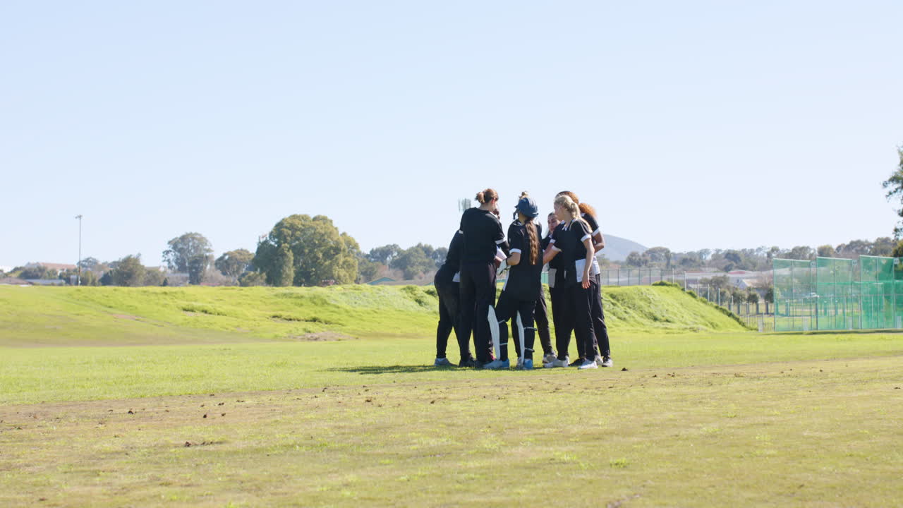 Female cricket team huddling on field, preparing for match on sunny day