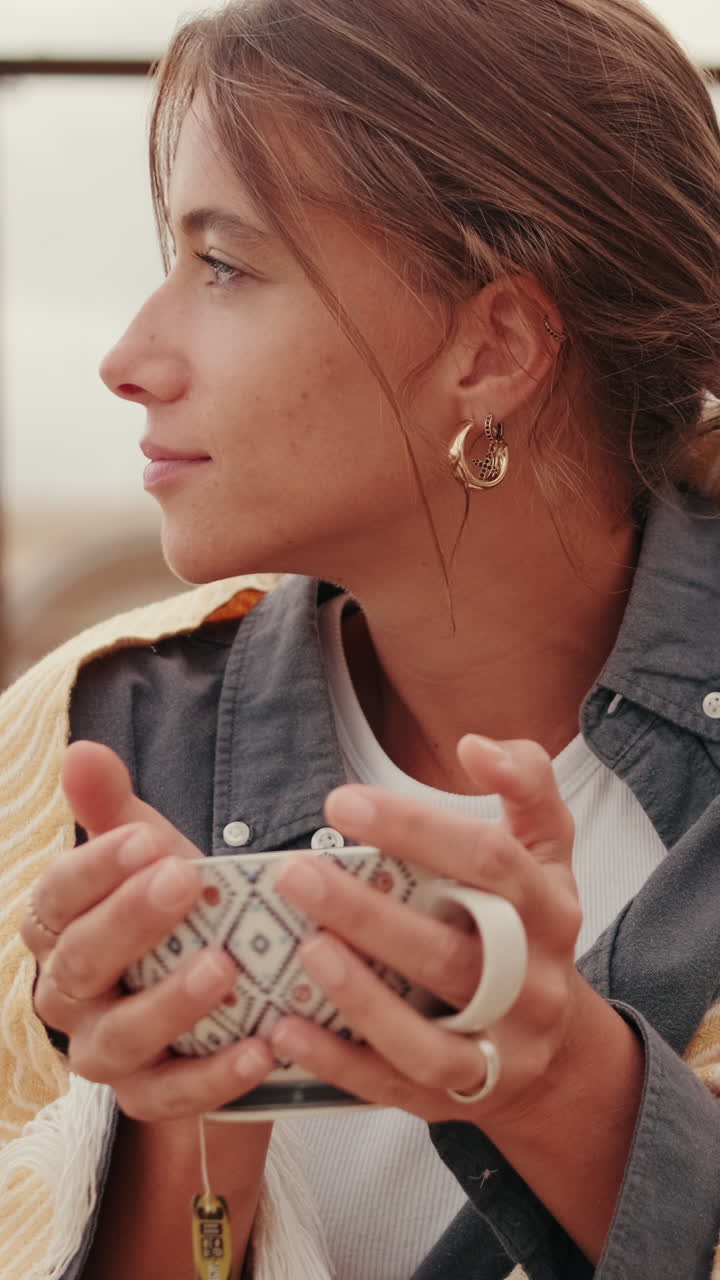 Giovane donna che tiene una tazza e guarda pensierosa all'aperto