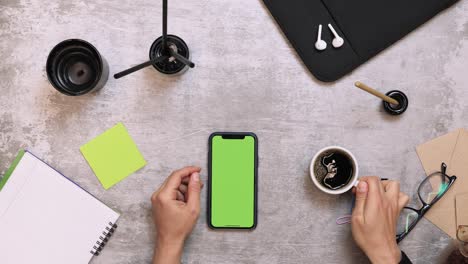 woman drinking coffee while sitting on desk at office. top view of office work desk with smartphone, supplies and cup of coffee. female works at work table with smartphone and drinks coffee