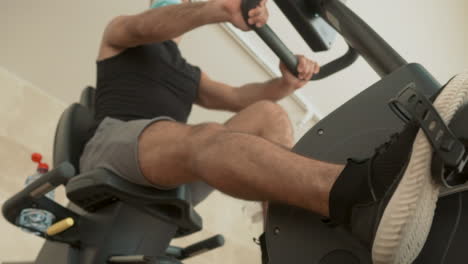 Athlete-Male-With-Face-Mask-Uses-A-Stationary-Bicycle-In-The-Gym