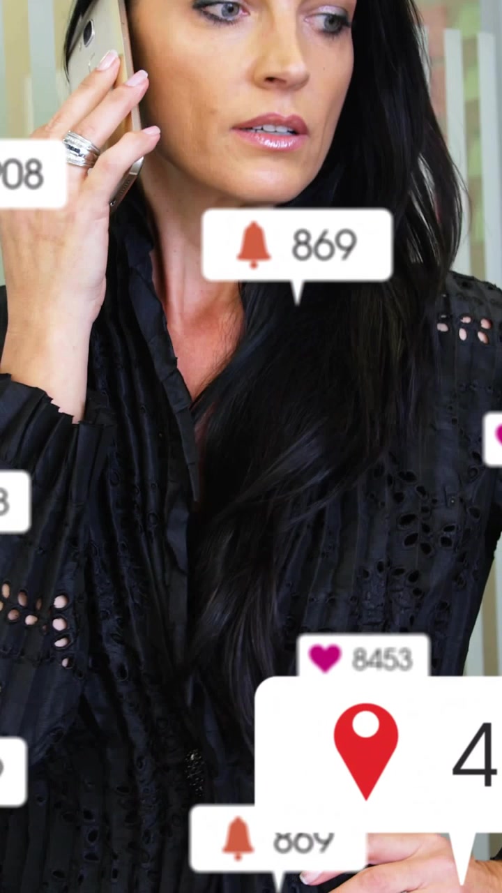 Video verticale: Donna al telefono che reagisce a notifiche e numeri che cambiano, in un contesto lavorativo per i media.