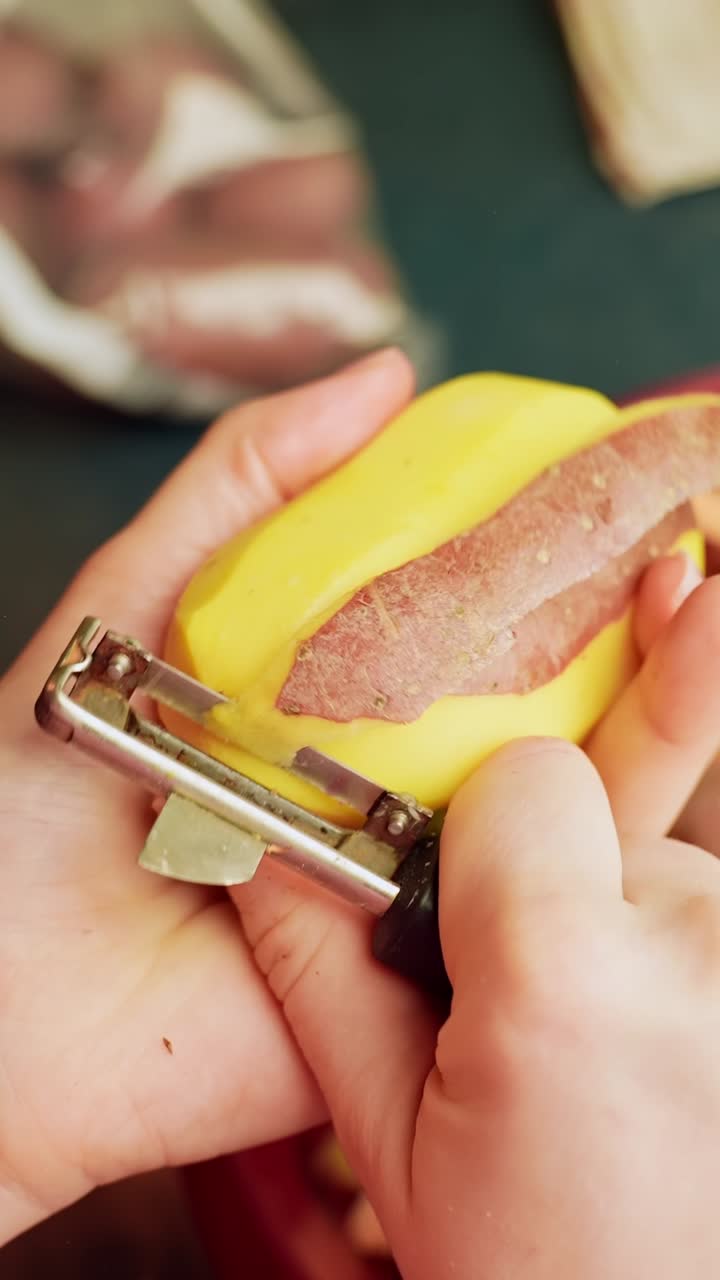 Vertical close-up of hands peeling a yellow potato with a metal peeler over a bowl, simple home cooking prep for dinner ingredients in a kitchen