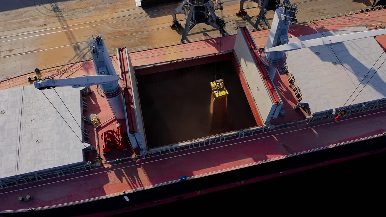 Drone, grain pouring from industrial bucket into ship hold during loading