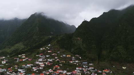 clouds over towering green mountains in the coastal town of seixal in northern madeira, portugal. aerial drone shot
