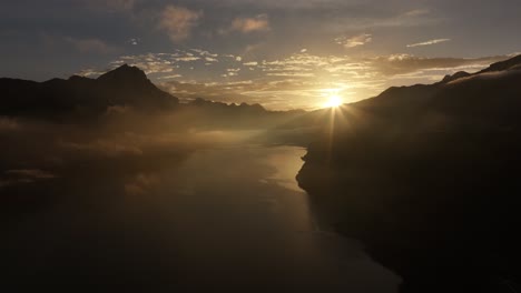 aerial view of lake walensee in switzerland at sunrise, with sun rays piercing through clouds and casting a warm glow over the serene lake and surrounding mountains.