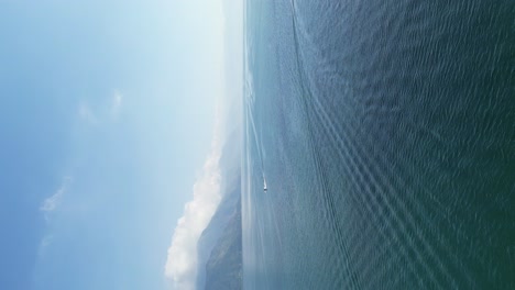 Drone-portrait-view-in-Guatemala-flying-over-a-blue-lake-surrounded-by-green-mountains-and-volcanos-on-a-cloudy-day-in-Atitlan