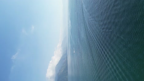 vista de retrato de avión no tripulado en guatemala volando sobre un lago azul rodeado de montañas verdes y volcanes en un día nublado en aitlan
