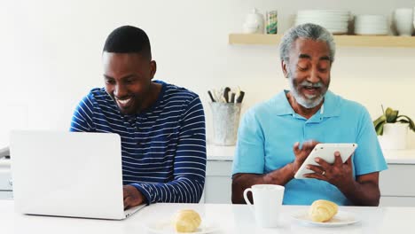 Father-and-son-using-laptop-and-digital-tablet-in-kitchen