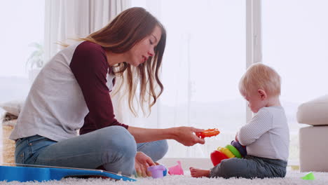 Madre-Joven-Sentada-En-El-Suelo-Jugando-Con-Su-Hijo-En-Casa