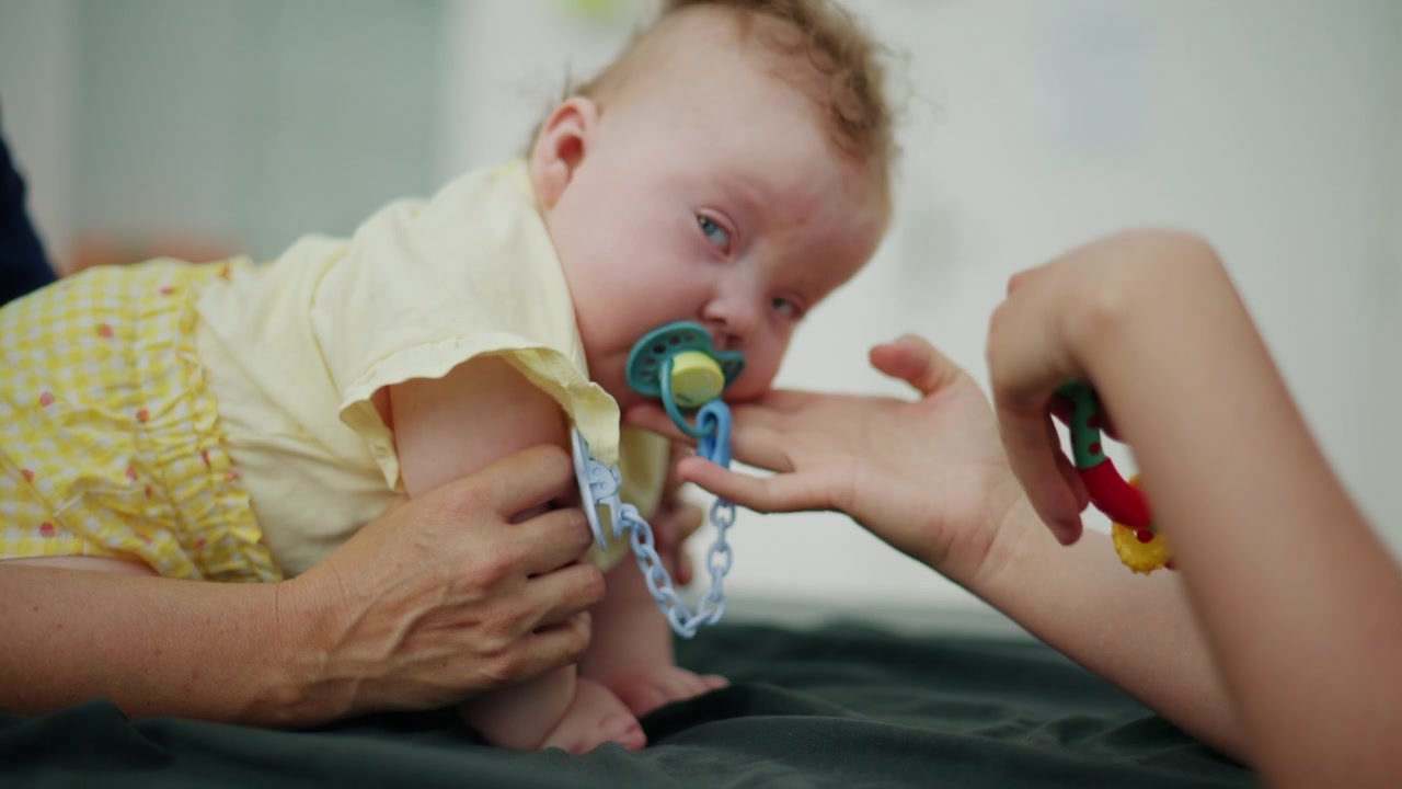 Adult hands supporting baby while offering a colorful teether toy, encouraging early childhood development and interaction