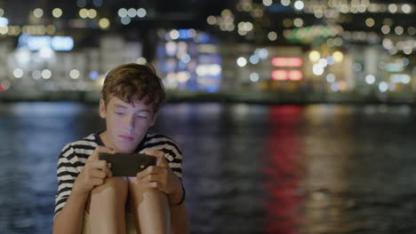 teenager playing game on smartphone by the water at night