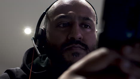 close up shot of a man wearing headphones listening to music using mobile phone while sitting inside a room