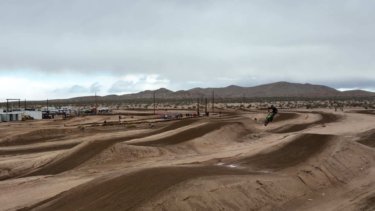 motocicleta dando un salto largo y alto desde una rampa de pista de tierra en un hipódromo todoterreno - antena de cámara lenta
