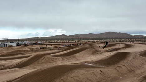 Motorcycle-taking-a-long-and-high-jump-off-a-dirt-track-ramp-on-an-off-road-racecourse---slow-motion-aerial