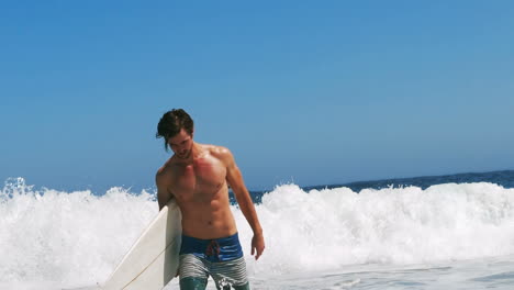 man getting out of water with surfboard