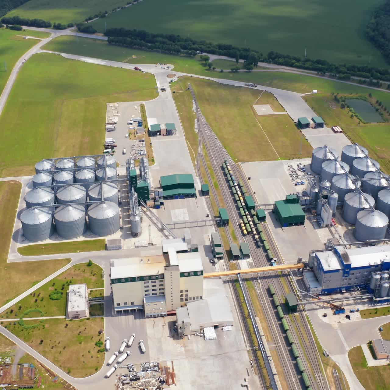 Modern agrocomplex on field. Grain elevators for storing crop. Large industrial territory with storage tanks. Freight trains on rails. Aerial view