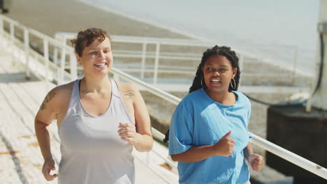 diverse cheerful women jogging along running track in park