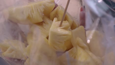 la mano de una mujer joven clava una rebanada de piña en un palo de bambú