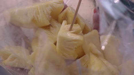 young woman hand impales pineapple slice on bamboo stick