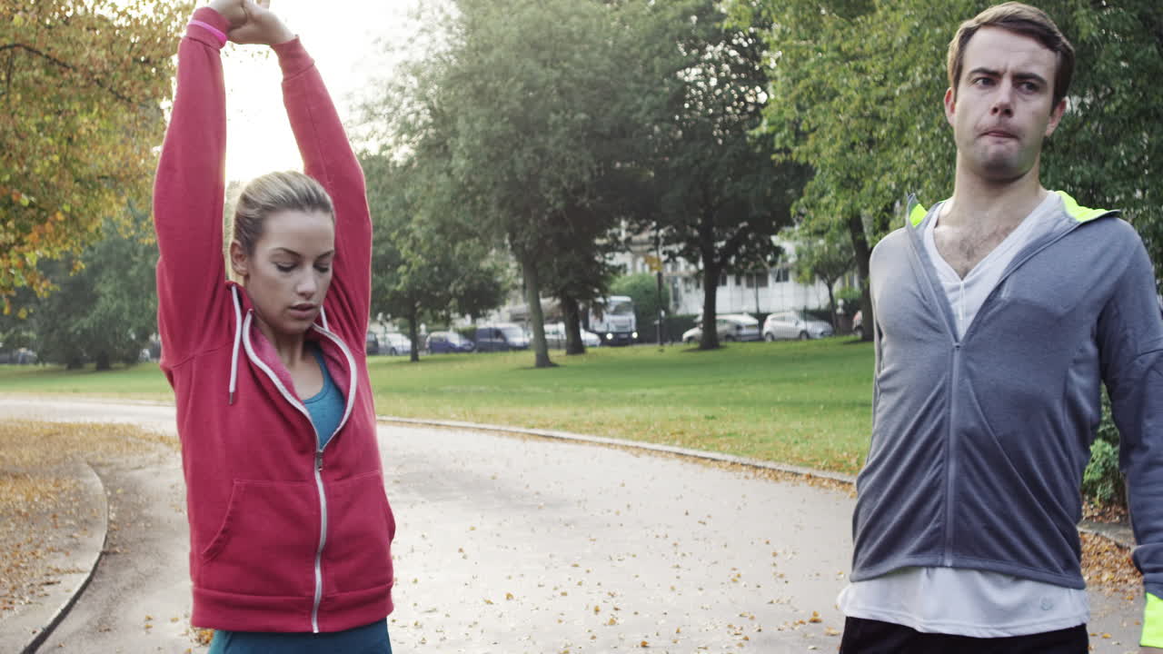 pareja atlética estirándose antes de correr en el parque usando dispositivos conectados a la tecnología portátil