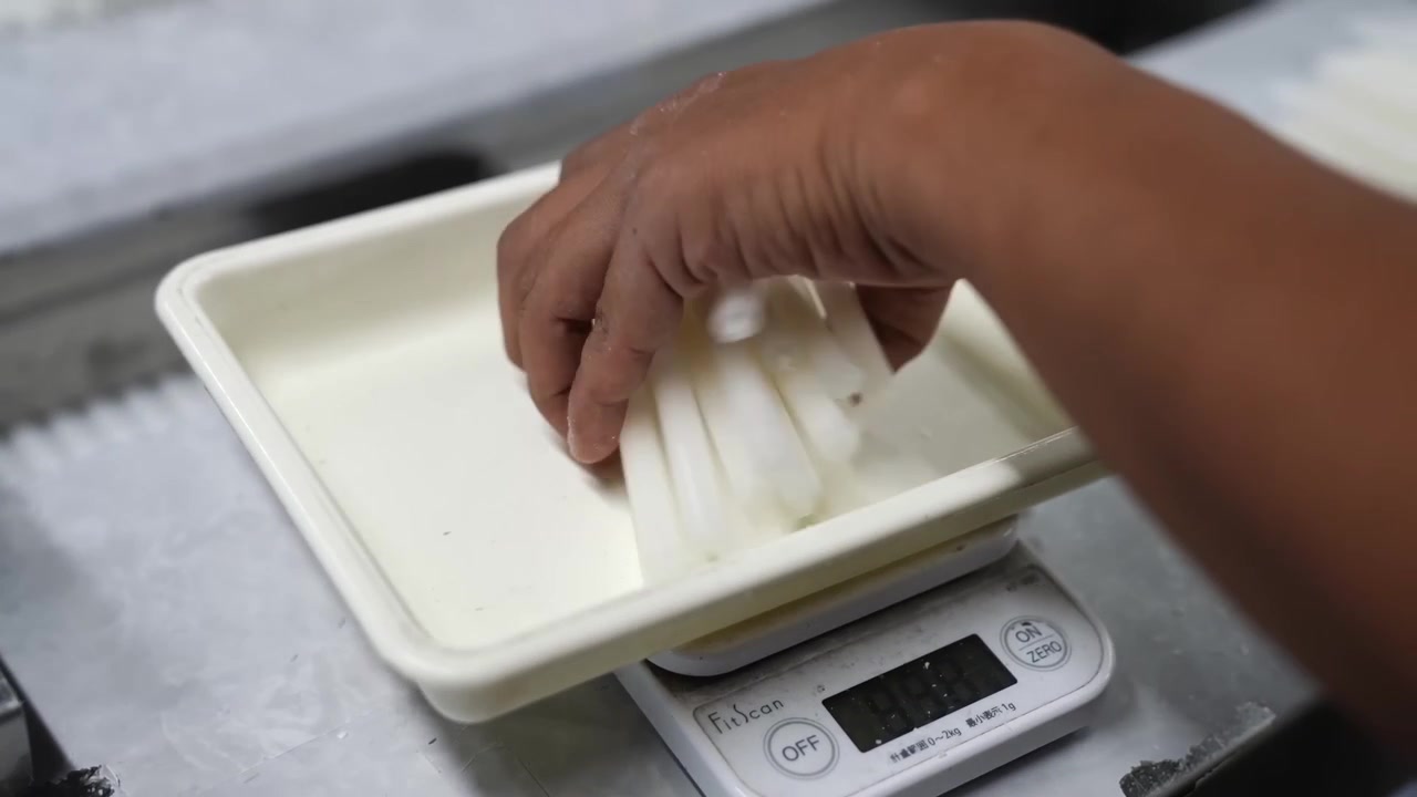 Operaio che posiziona un vassoio su una bilancia digitale per pesare il materiale per candele in una fabbrica
