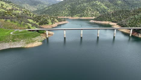 golden california hills frame the don pedro reservoir bridge in this aerial drone shot. shot on an air 3s.