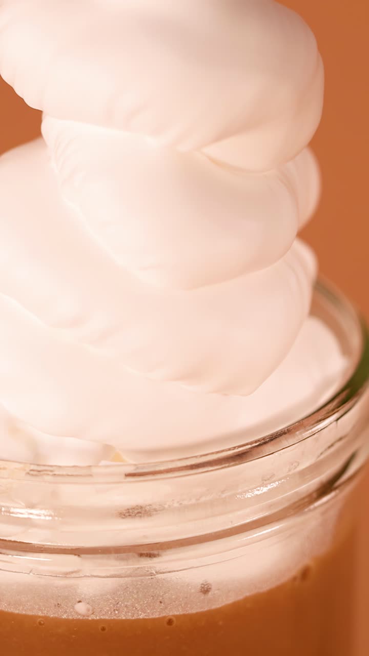Panna montata liscia forma spirali su un cremoso milkshake al cioccolato in primo piano, illuminazione calda da studio, telecamera fissa