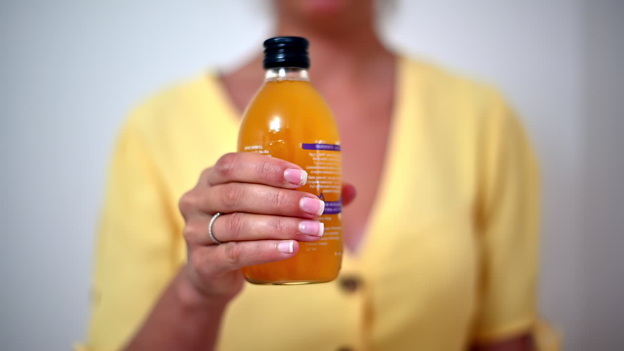 A person is holding a bottle of a bright orange drink in a well-lit room. The drink appears refreshing and is likely made from healthy ingredients. The atmosphere feels uplifting