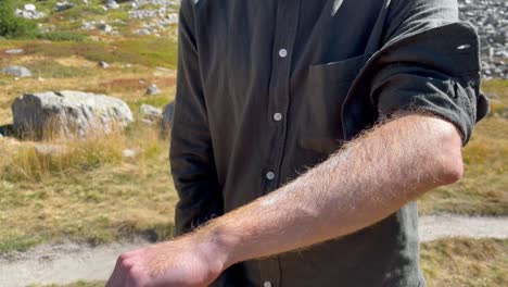 a red boy puts sunscreen in his arm pre protect himself from the sun's rays, in the background a mountain landscape