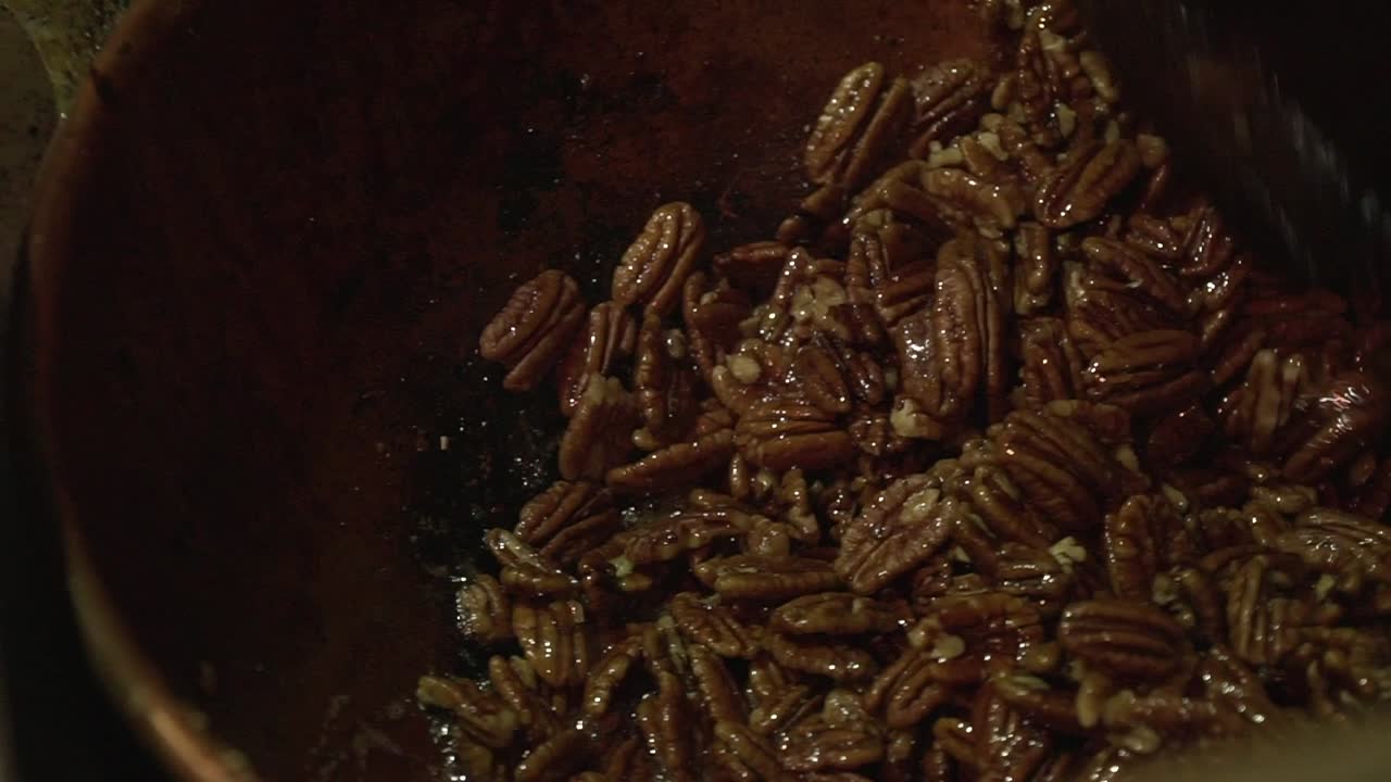 cerrar la toma en cámara lenta de nueces de pecan caramelizadas tostadas que se agitan con una gran paleta de madera